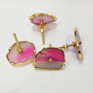 Op de afbeelding: Drie roze en witte agaat-ladegrepen met gouden rand. De grepen hebben een unieke, natuurlijke vorm en zijn perfect om elke woning een vleugje elegantie te geven.