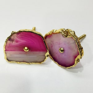 Op de afbeelding: Twee roze en witte agaat-ladegrepen met gouden metalen accenten. De agaat is een natuursteen met een uniek patroon.