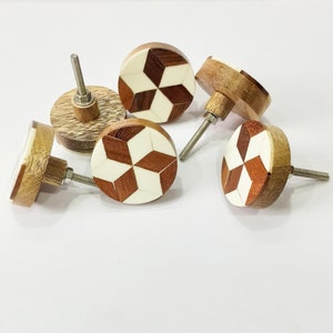 May include: Set of five wooden cabinet knobs with a geometric pattern of white and brown wood. The knobs have a round shape and a metal screw for attaching to a cabinet door.