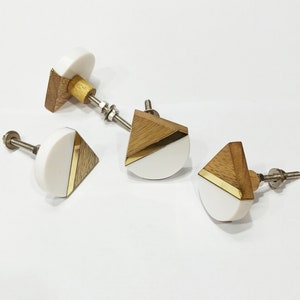 Puede incluir: Conjunto de cuatro pomos de armario de madera y blanco con detalles dorados. Cada pomo presenta un diseño geométrico con forma de semicírculo y un triángulo.