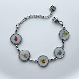 May include: Silver-toned bracelet featuring round charms with colorful illustrations of a ladybug, snail, bee, butterfly, and bird. The bracelet has a chain extension and a lobster clasp for secure wear.