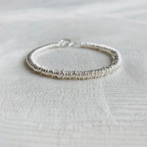 May include: A silver bracelet with a textured, coiled design. The bracelet is circular and features a clasp closure. The metal has a bright, reflective quality, and the design gives it a unique, handmade appearance.