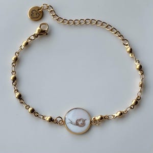 Könnte beinhalten: Goldfarbenes Armband mit einem Schneckenmotiv auf einem runden Anhänger. Das Armband hat ein filigranes Kettendesign mit kleinen, runden Perlen und einem Karabinerverschluss. Ein kleiner Anhänger mit einem Herz und der Zahl 3 ist ebenfalls angebracht.