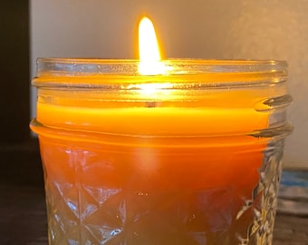 May include: A clear glass jar candle with a yellow and orange wax blend. The candle is lit and the flame is visible.