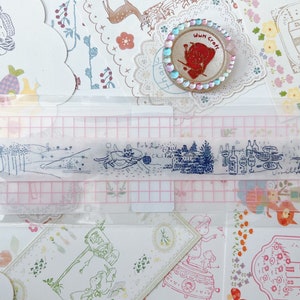 May include: A clear plastic sheet with a grid pattern and several blue ink stamps of various scenes, including a house, a forest, and a group of people. The sheet is on a background of colorful paper with various designs.