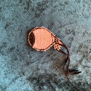 Peut inclure: Un cache-œil en feutre rose et marron avec une pupille en feutre noir. Le cache-œil est doté d'une ficelle en feutre marron.