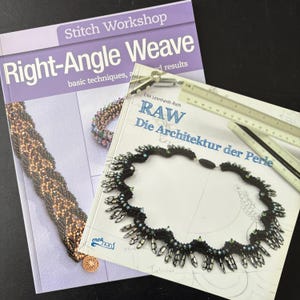 Könnte beinhalten: Zwei Bücher über Perlenarbeitstechniken. Das Buch links trägt den Titel "Stitch Workshop Right-Angle Weave" mit einem lila Einband. Das Buch rechts trägt den Titel "RAW Die Architektur der Perle". Eine Perlenkette und ein Lineal sind ebenfalls zu sehen.