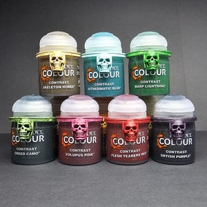 May include: A collection of Citadel Contrast paints in various colors, including green, blue, and purple. Each paint pot has a skull-shaped accent and a label indicating the color name, such as "Skeleton Horde" and "Warp Lightning."
