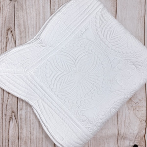 May include: White quilted throw blanket with a floral pattern. The blanket has a scalloped edge and is made of a soft, comfortable fabric.