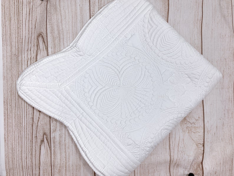 May include: White quilted throw blanket with a floral pattern. The blanket has a scalloped edge and is made of a soft, comfortable fabric.