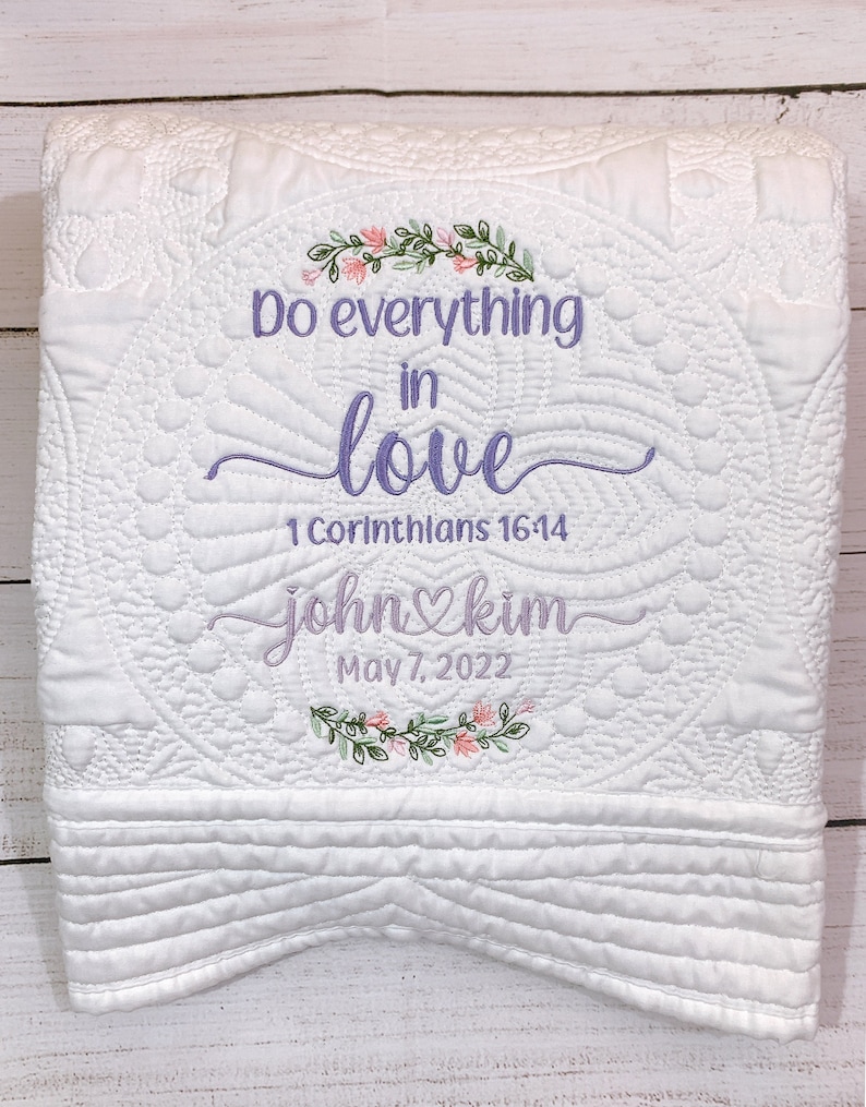 May include: White quilted blanket with embroidered floral designs and the text "Do everything in love 1 Corinthians 16:14 john&kim May 7, 2022".