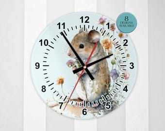 May include: A round wall clock with a light blue background featuring a watercolor illustration of a brown mouse holding small flowers. The clock has black numbers, black hour and minute hands, a red second hand, and a circular badge stating 8 DESIGNS AVAILABLE.