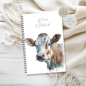 Könnte beinhalten: Ein spiralgebundenes Notizbuch mit einer Aquarellillustration eines Kuhgesichts auf dem Cover. Auf dem Cover steht "Kim's Notebook" in Schreibschrift. Kreisförmige Grafiken weisen auf weitere Designoptionen und Textanpassung hin.