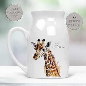 Könnte beinhalten: Weißer Keramikkrug mit einer Giraffenillustration. Die Giraffe hat braune und beige Flecken und ist mit "Jessie" beschriftet. Der Krug hat einen gebogenen Griff und den Text "Add Your Own Text" und "8 Designs Available" auf den Seiten.