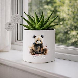 May include: A white ceramic planter with a watercolor panda bear design. The panda is sitting with its legs crossed, and the planter has the text "Your Text" in cursive. The planter holds a green succulent plant. The image also includes text that says "Add Your Own Text" and "8 Designs Available".