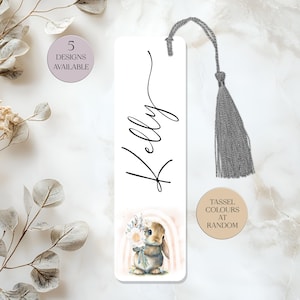 May include: White bookmark featuring the name "Kelly" in black script, with a watercolour illustration of a bunny holding flowers. It has a grey tassel and text that says "5 Designs Available".