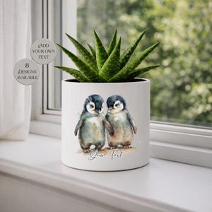 May include: White ceramic planter with a watercolor illustration of two penguins holding hands. The planter contains a green succulent plant. Text on the planter reads "Your Text". Additional text on the left side says "Add Your Own Text" and "8 Designs Available".