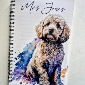 May include: A spiral-bound notebook featuring a watercolour illustration of a brown and tan dog. The cover displays the name "Mrs Jones" in cursive script, with a colourful watercolour splash design.