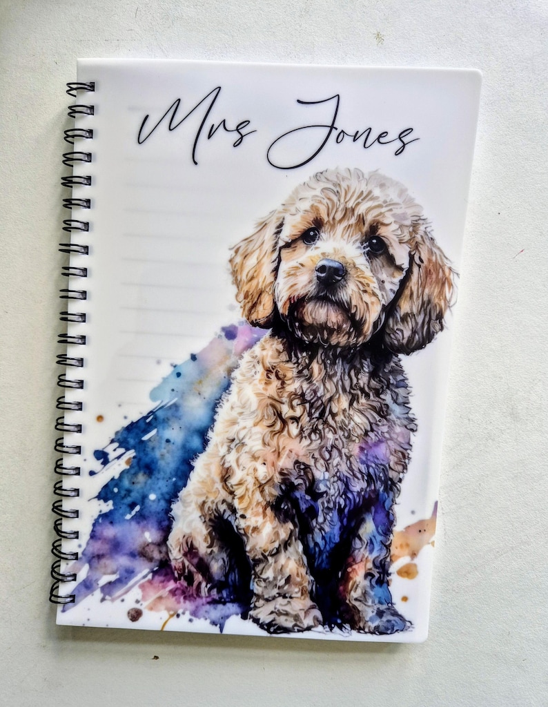May include: A spiral-bound notebook featuring a watercolour illustration of a brown and tan dog. The cover displays the name "Mrs Jones" in cursive script, with a colourful watercolour splash design.