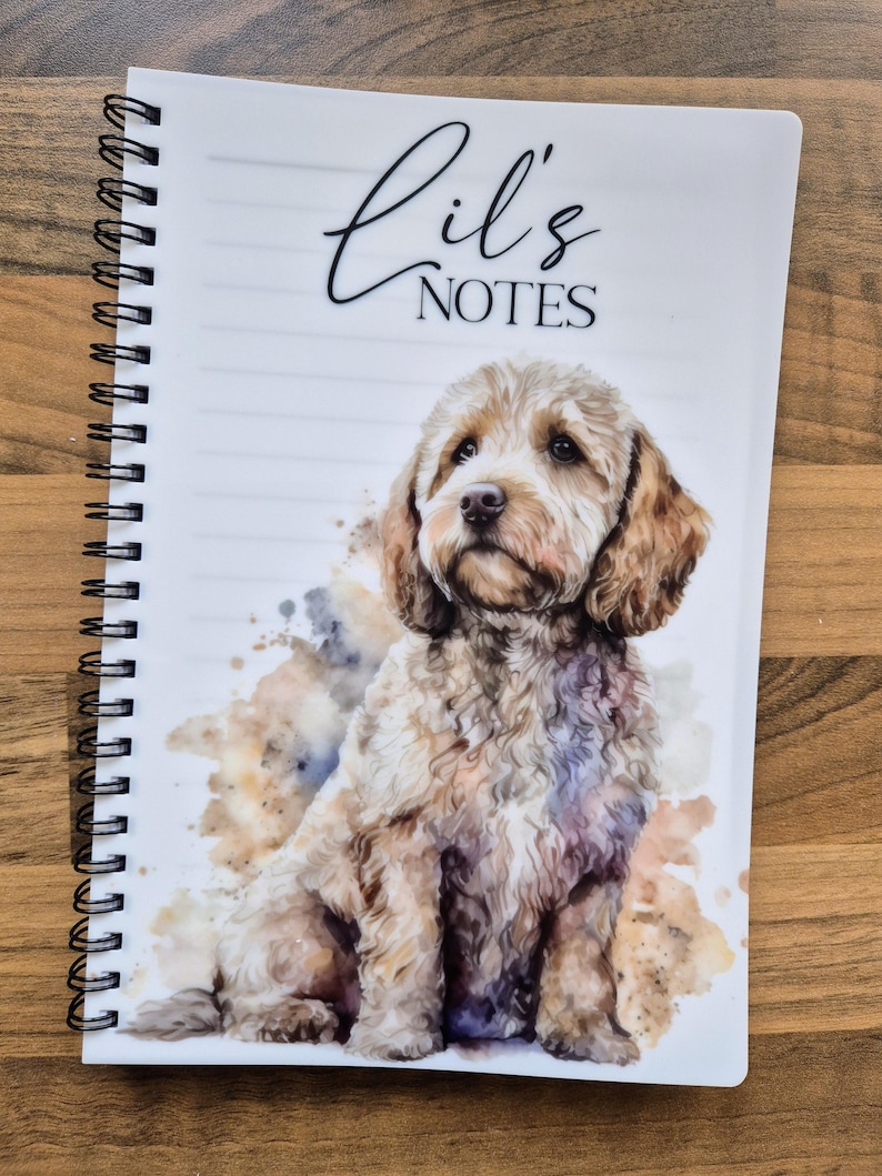 May include: A spiral-bound notebook with a watercolour illustration of a light brown dog. The cover reads "Lil's NOTES" in script. The notebook has lined pages and a white cover, perfect for jotting down notes.