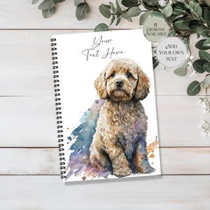 May include: A spiral-bound notebook with a watercolour illustration of a light brown dog. The notebook features the text "Your Text Here" and a watercolour splash in blue, purple, and gold. Additional text indicates "8 Designs Available" and "Add Your Own Text".