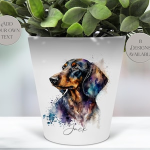 May include: White ceramic planter featuring a watercolor-style illustration of a dachshund dog. The dog is depicted in shades of black, brown, and blue with the name "Jack" written below. The planter has the text "Add Your Own Text" and "8 Designs Available".
