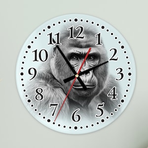 May include: A round wall clock featuring a detailed grayscale image of a gorilla's face. The clock has black numerals, black hands, and a red second hand. The clock face is surrounded by a light blue border with black dots.