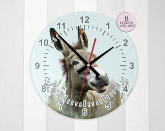 May include: A round wall clock featuring a photographic print of a brown donkey against a light blue background with floral elements. The clock face displays black numbers from 1 to 12, black hour and minute hands, a red second hand, and a circular badge stating 8 DESIGNS AVAILABLE.