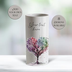 May include: A white cylindrical vase featuring a watercolour heart-shaped tree design in pinks, purples, greens, and blues. The text "Your text here" is on the vase. Two circles with text are on either side of the vase.