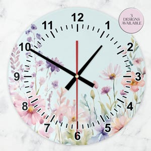 Könnte beinhalten: Eine runde Wanduhr mit hellblauem Zifferblatt mit einem Blumendesign in Rosa, Lila und Weiß. Die Uhr hat schwarze Zahlen und Zeiger mit einem roten Sekundenzeiger. Der Text "3 DESIGNS AVAILABLE" befindet sich in einem rosa Kreis.