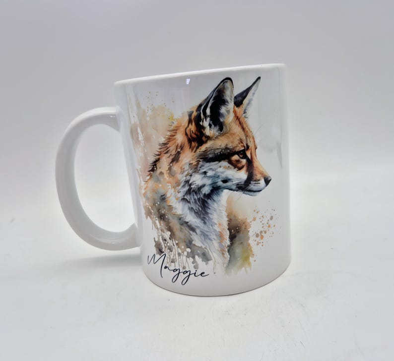 May include: White ceramic mug featuring a watercolor illustration of a fox in shades of brown, orange, and white. The mug has a curved handle and the name "Maggie" is written in cursive.