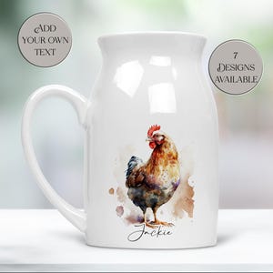May include: A white ceramic pitcher with a large handle, featuring a watercolor painting of a rooster. The rooster is brown, red, and blue, with the name "Jackie" written below. Two circular text elements read "Add Your Own Text" and "7 Designs Available".