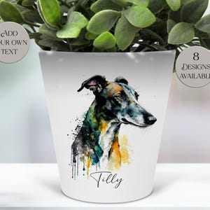 Peut inclure: Pot de fleurs en céramique blanche avec une peinture à l'aquarelle d'un lévrier. Le portrait du chien comprend des éclaboussures de peinture noire, bleue, jaune et orange. Le nom "Tilly" est écrit en dessous. Le texte sur le pot indique "Add Your Own Text" et "8 Designs Available."