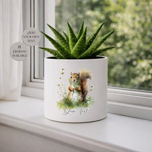 May include: White ceramic planter with a watercolor illustration of a squirrel holding flowers. The planter has a green succulent plant inside. Text on the planter reads "Your Text". Two circular graphics on the left side say "Add Your Own Text" and "8 Designs Available".