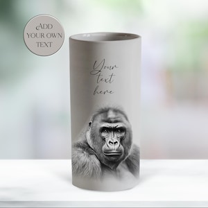 May include: A cylindrical, light gray ceramic mug featuring a detailed black and white illustration of a gorilla's face. The mug has the text "Your text here" in cursive and a circular graphic that says "Add your own text".
