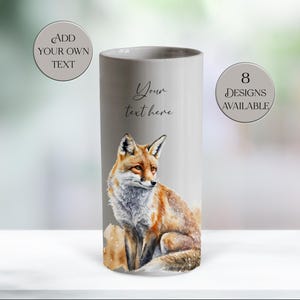 May include: A grey ceramic vase with a watercolour fox illustration. The vase has the text "Your text here", "Add your own text" and "8 designs available" in a circular design. The fox has orange and white fur.