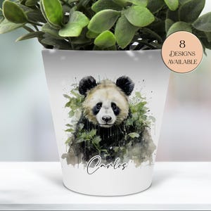 May include: White ceramic plant pot with a watercolour panda bear design. The panda is surrounded by green foliage and the name "Carlos" is written in script. A circular sticker indicates "8 Designs Available".