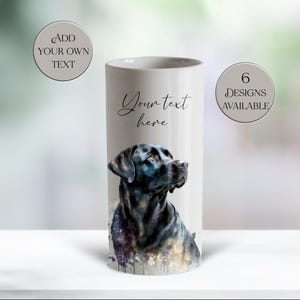 May include: A white cylindrical tumbler featuring a watercolour-style illustration of a black Labrador retriever. The text "Your text here" is printed above the dog. Two circular badges state "ADD YOUR OWN TEXT" and "6 DESIGNS AVAILABLE".
