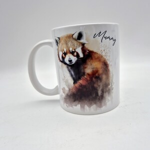 Puede incluir: Una taza de cer&aacute;mica blanca con una ilustraci&oacute;n en acuarela de un panda rojo con pelaje marr&oacute;n, negro y blanco. La palabra Mummy est&aacute; impresa en letra cursiva negra a la derecha del panda rojo. La taza tiene un asa curva en el lado izquierdo.