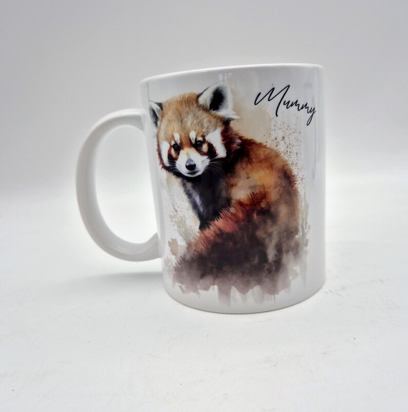 Puede incluir: Una taza de cer&aacute;mica blanca con una ilustraci&oacute;n en acuarela de un panda rojo con pelaje marr&oacute;n, negro y blanco. La palabra Mummy est&aacute; impresa en letra cursiva negra a la derecha del panda rojo. La taza tiene un asa curva en el lado izquierdo.
