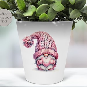 May include: White ceramic plant pot featuring a watercolour illustration of a gnome wearing a pink knitted hat and holding a heart. The heart has the name "Jessica" on it. The pot has the text "Add Your Own Text" on it.