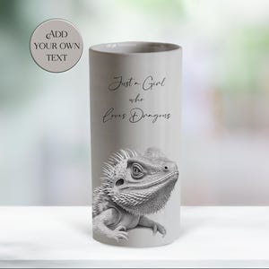 Peut inclure: Mug cylindrique en céramique gris clair avec une illustration en noir et blanc d'un dragon barbu. Le mug porte l'inscription "Just a Girl who Loves Dragons" en écriture cursive. Un graphique circulaire au-dessus du mug indique "Add Your Own Text".