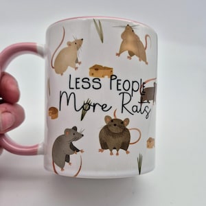May include: White ceramic mug with a pink handle and rim, decorated with cartoon rats and cheese illustrations. The mug displays the text "LESS PEOPLE More Rats" in black script.