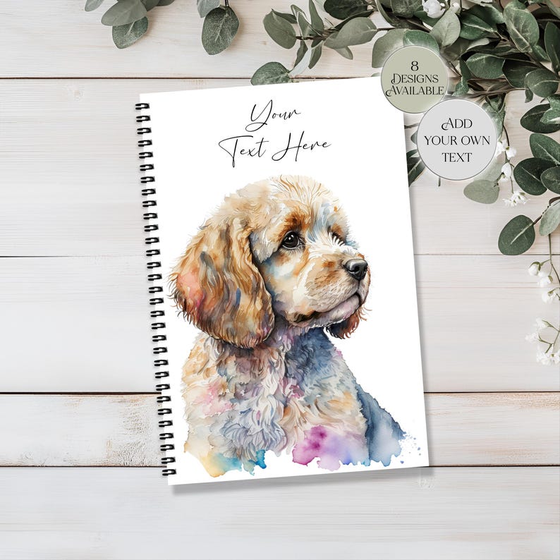 May include: A spiral-bound notebook with a watercolour illustration of a Cocker Spaniel. The dog has tan and white fur with colourful accents. The notebook cover has the text "Your Text Here" and design options.