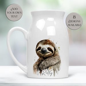May include: White ceramic jug with a large handle, featuring a watercolour illustration of a sloth. The sloth is brown and tan with a smiling face. The jug has the text "Kelly" below the sloth.