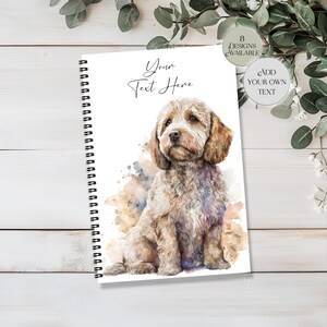 May include: A spiral-bound notebook with a watercolour illustration of a Cockapoo dog. The dog is light brown with a fluffy coat, set against watercolour splashes. The text "Your Text Here" is displayed above the dog. Additional text indicates "8 Designs Available" and "Add Your Own Text".