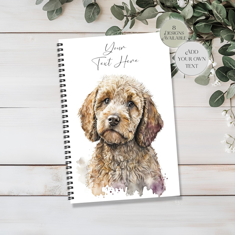 May include: A spiral-bound notebook with a watercolour illustration of a brown and tan Goldendoodle dog. The cover has the text "Your Text Here" in script. Additional text indicates "8 Designs Available" and "Add Your Own Text".