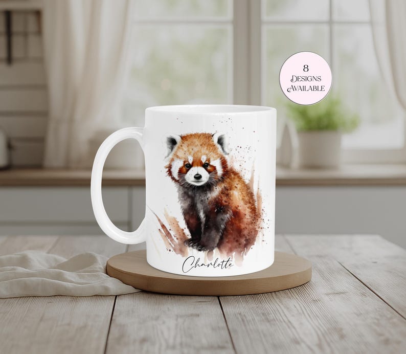 Personalised red panda mug featuring a charming watercolour illustration of a red panda with rich orange and brown fur, customised with the name “Charlotte”. White ceramic wildlife mug displayed on a wooden stand in a cosy home setting. A thoughtful personalised gift for red panda lovers, animal enthusiasts and nature lovers, perfect for birthdays, Christmas, Mother’s Day or special occasions. Eight designs available.