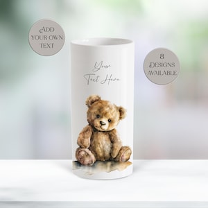 May include: A white cylindrical tumbler featuring a watercolour illustration of a brown teddy bear sitting down. The text "Your Text Here" is printed above the bear. Two circular badges state "ADD YOUR OWN TEXT" and "8 DESIGNS AVAILABLE".