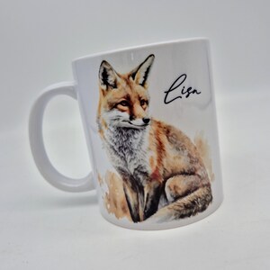 May include: White ceramic mug featuring a watercolor illustration of a fox in shades of brown, orange, and white. The mug has a curved handle and the name "Lisa" in black script.
